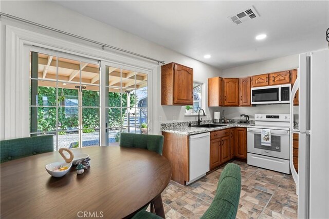 kitchen featuring light stone counters, white appliances, and sink