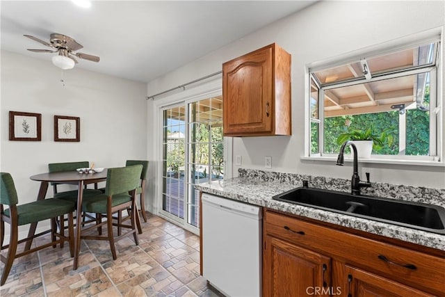 kitchen featuring brown cabinetry, plenty of natural light, dishwasher, and a sink