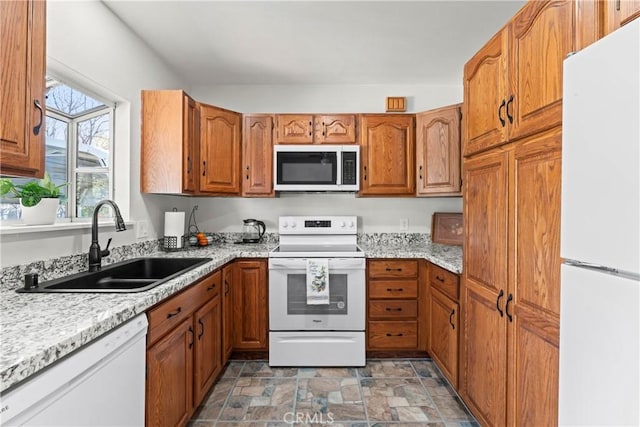 kitchen featuring stone finish flooring, white appliances, brown cabinetry, and a sink