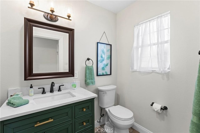 half bath featuring baseboards, vanity, and toilet