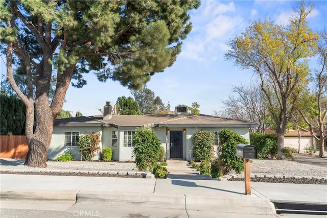 ranch-style house featuring a chimney, fence, and stucco siding