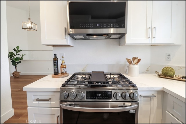 kitchen featuring stainless steel appliances, white cabinetry, light stone countertops, and extractor fan