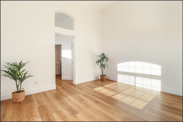 unfurnished room with a towering ceiling and light wood-type flooring