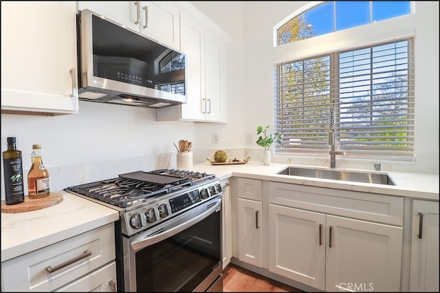 kitchen featuring sink, light hardwood / wood-style flooring, appliances with stainless steel finishes, light stone countertops, and white cabinets