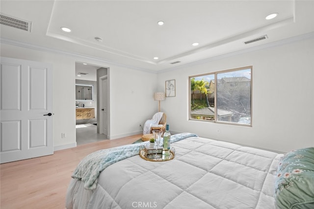 bedroom featuring ornamental molding, connected bathroom, a raised ceiling, and light wood-type flooring