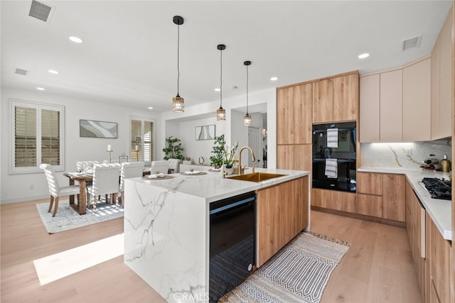 kitchen featuring sink, light stone counters, black appliances, light hardwood / wood-style floors, and a center island with sink