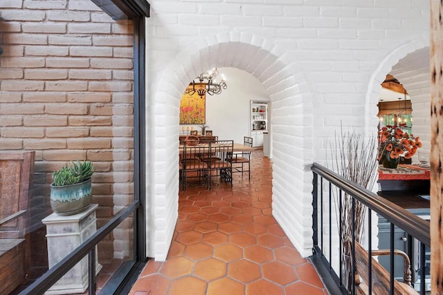 corridor with an inviting chandelier, tile patterned flooring, and brick wall