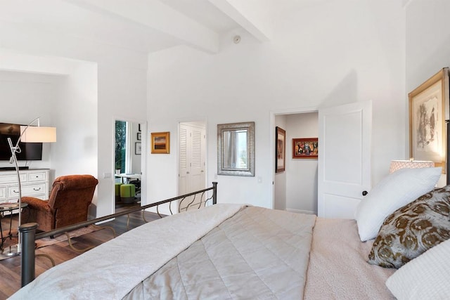 bedroom with beamed ceiling, wood-type flooring, and a high ceiling