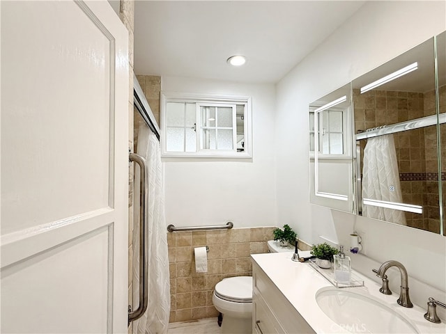 bathroom with tile walls, vanity, a shower with shower door, and toilet