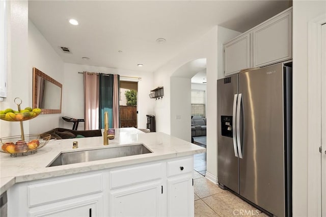 kitchen with light tile patterned floors, sink, light stone counters, white cabinets, and stainless steel fridge with ice dispenser