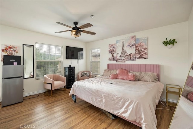 bedroom with hardwood / wood-style flooring, ceiling fan, stainless steel fridge, and multiple windows