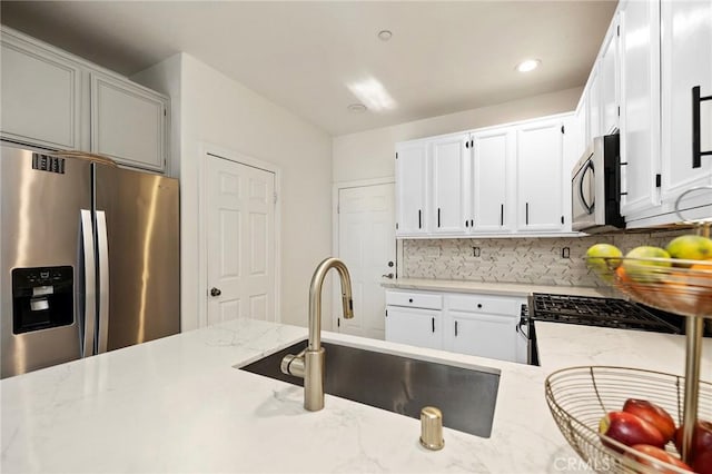 kitchen with white cabinetry, appliances with stainless steel finishes, sink, and light stone counters