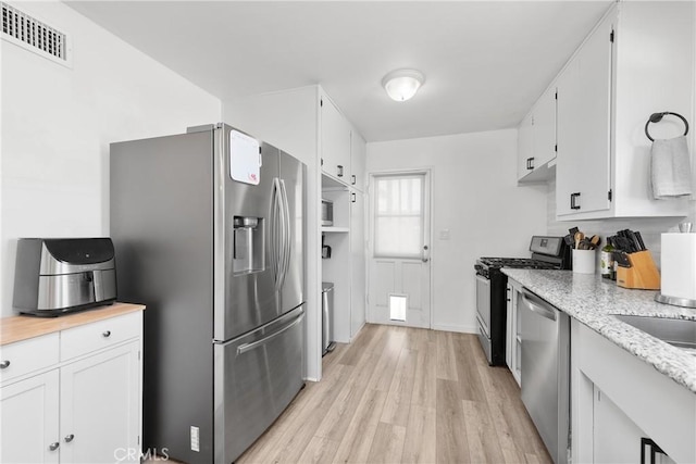 kitchen with white cabinetry, stainless steel appliances, and light hardwood / wood-style flooring