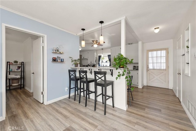 kitchen featuring white cabinets, a kitchen bar, decorative light fixtures, kitchen peninsula, and light wood-type flooring