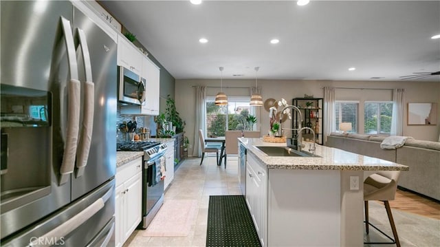 kitchen with sink, white cabinetry, hanging light fixtures, stainless steel appliances, and an island with sink