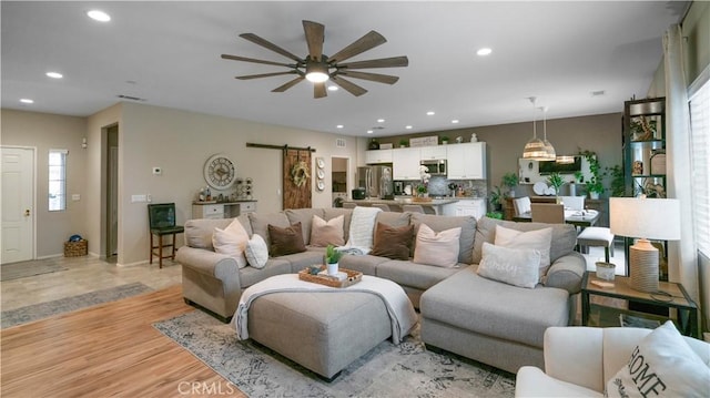 living room featuring light hardwood / wood-style floors, a barn door, and ceiling fan