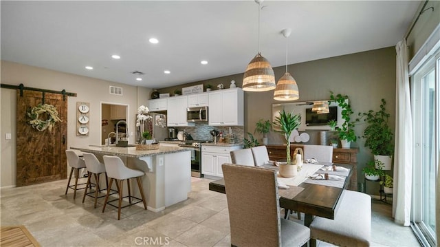 kitchen featuring appliances with stainless steel finishes, white cabinetry, hanging light fixtures, a center island with sink, and a barn door