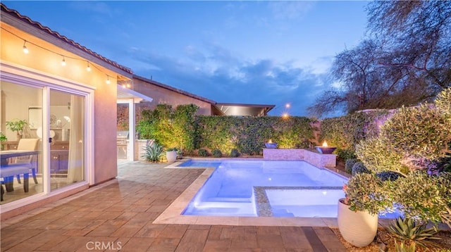 pool at dusk with a patio area and an in ground hot tub