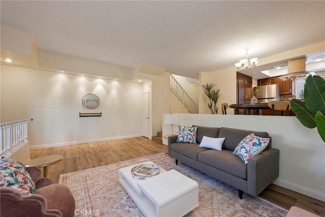 living area with light wood-style flooring, stairway, an inviting chandelier, a textured ceiling, and baseboards