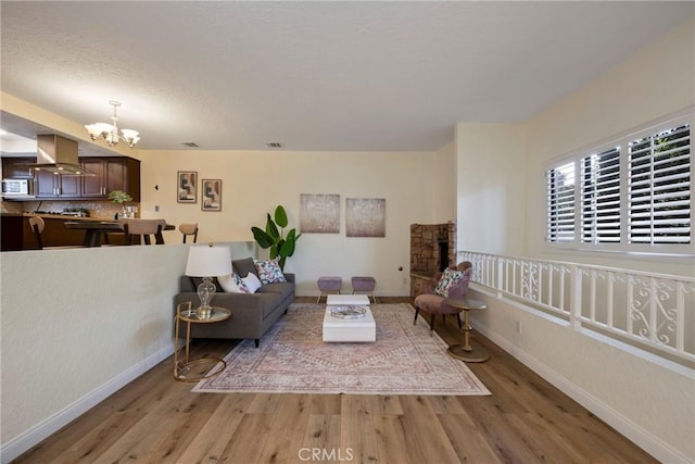 living area featuring visible vents, baseboards, light wood-style floors, a fireplace, and a notable chandelier