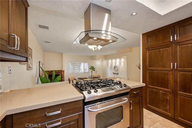 kitchen featuring light countertops, wall chimney range hood, a textured ceiling, gas range, and a chandelier