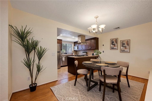 dining area featuring a textured ceiling, light wood-style flooring, visible vents, baseboards, and an inviting chandelier