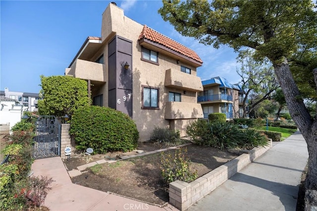 exterior space featuring a tile roof, a gate, and stucco siding