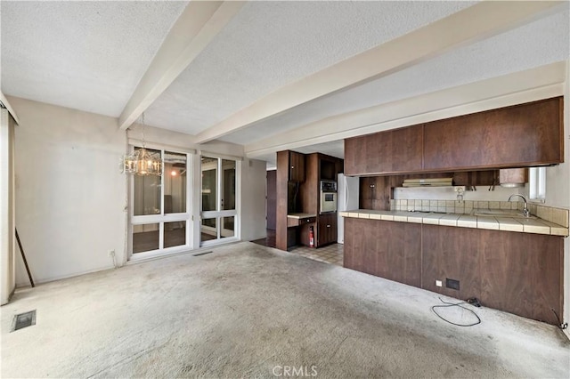 kitchen featuring sink, beam ceiling, tile counters, light carpet, and oven