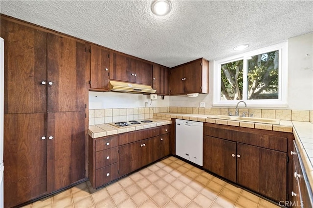 kitchen featuring dark brown cabinetry, sink, tile countertops, a textured ceiling, and white appliances