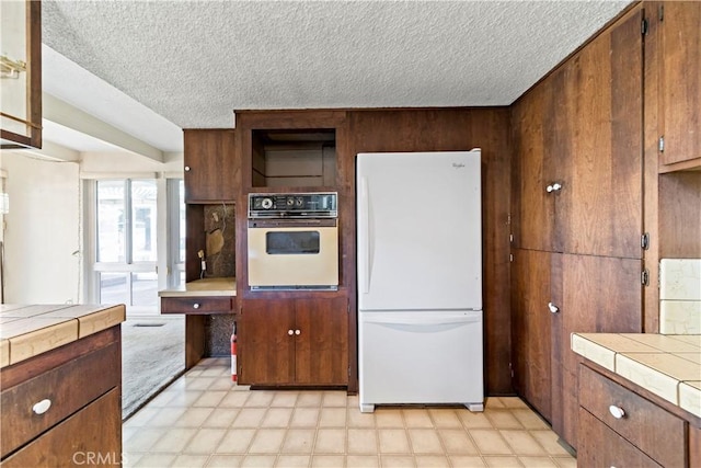 kitchen with wooden walls, white refrigerator, tile counters, a textured ceiling, and oven