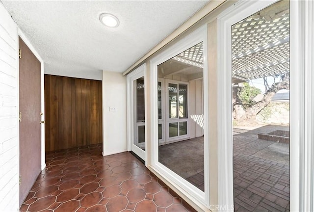 entryway with dark tile patterned flooring, wooden walls, and a textured ceiling