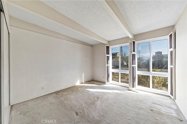 empty room featuring light carpet, a wealth of natural light, beamed ceiling, and a textured ceiling