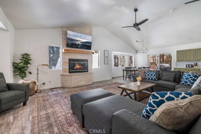 living room featuring hardwood / wood-style floors, ceiling fan with notable chandelier, a fireplace, and high vaulted ceiling