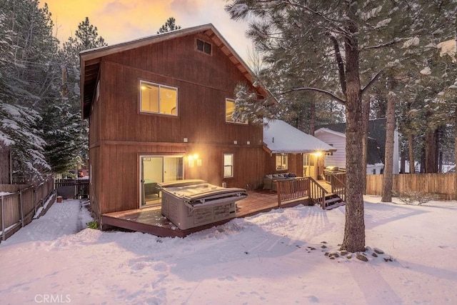 snow covered back of property featuring a jacuzzi and a deck