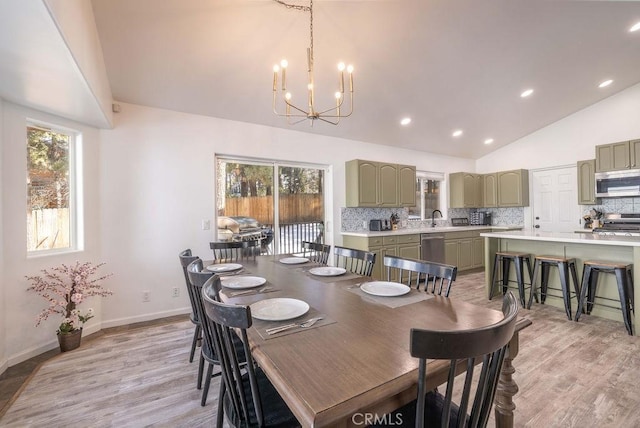 dining space with a notable chandelier, high vaulted ceiling, sink, and light wood-type flooring