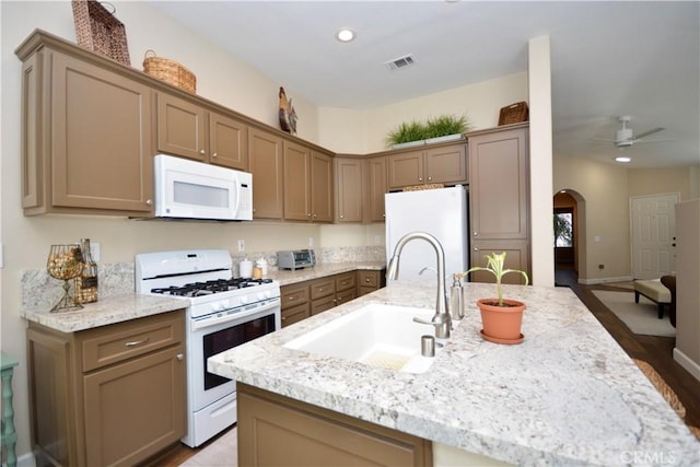 kitchen with sink, light stone counters, a kitchen island with sink, and white appliances