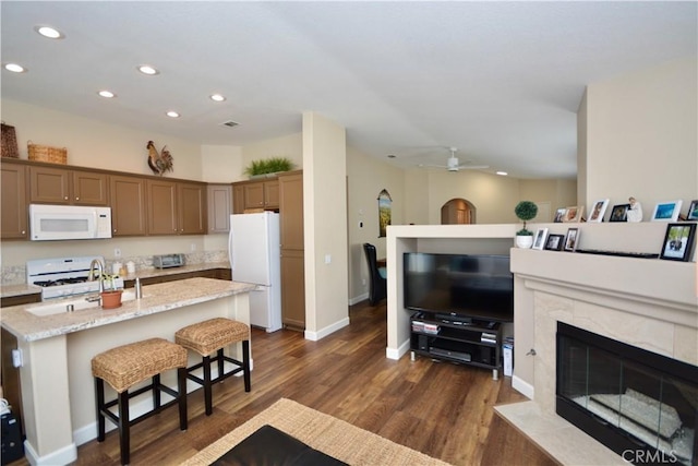 kitchen with an island with sink, a kitchen bar, light stone counters, a premium fireplace, and white appliances