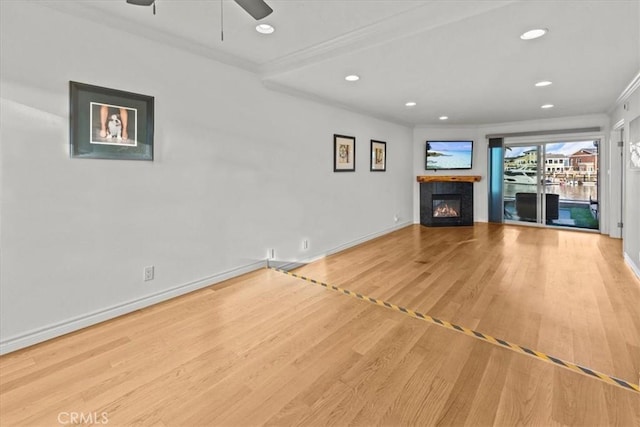 unfurnished living room with crown molding, ceiling fan, a tiled fireplace, and light hardwood / wood-style flooring