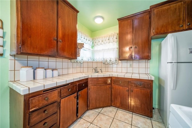 kitchen featuring sink, tasteful backsplash, tile countertops, light tile patterned floors, and white refrigerator