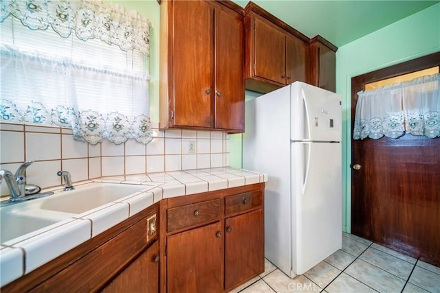 kitchen featuring sink, backsplash, white fridge, tile counters, and light tile patterned floors