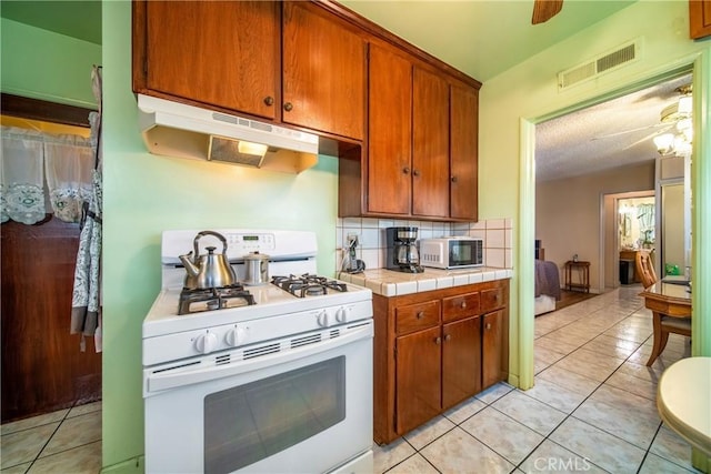 kitchen featuring decorative backsplash, ceiling fan, tile counters, and gas range gas stove