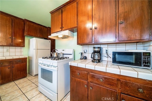 kitchen with tasteful backsplash, light tile patterned floors, white appliances, and tile counters