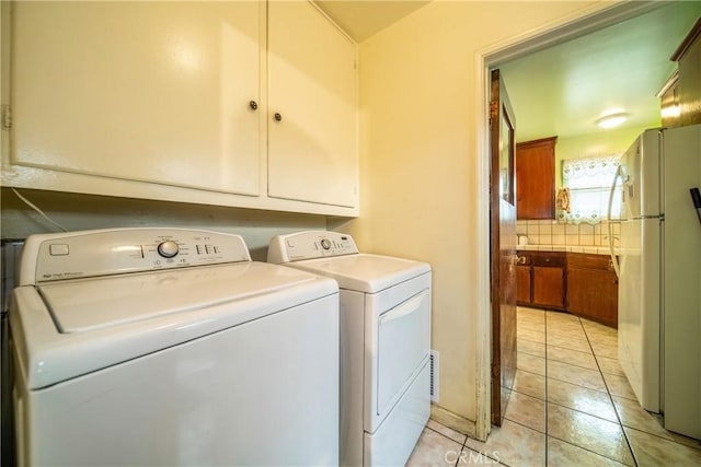 laundry area featuring washing machine and dryer, cabinets, and light tile patterned flooring