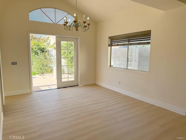 empty room with vaulted ceiling, an inviting chandelier, and light hardwood / wood-style flooring