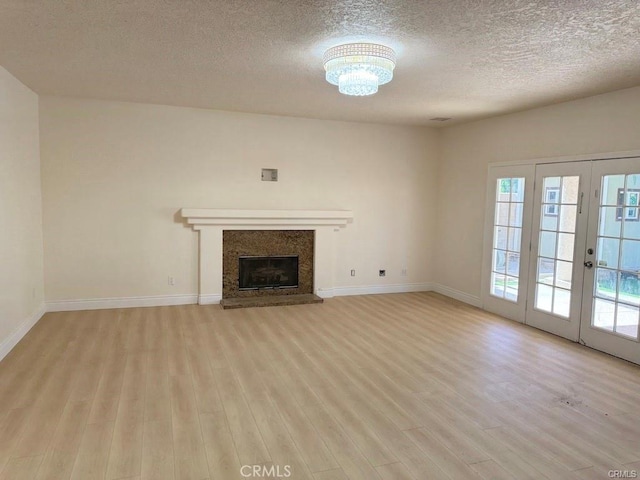 unfurnished living room featuring a textured ceiling, light wood-type flooring, and french doors