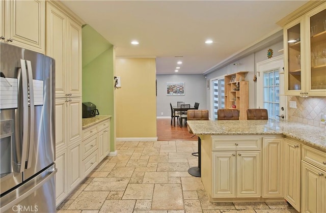 kitchen featuring stainless steel refrigerator with ice dispenser, light stone countertops, kitchen peninsula, and cream cabinetry