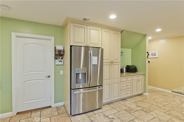 kitchen featuring light stone countertops, stainless steel fridge, and cream cabinetry