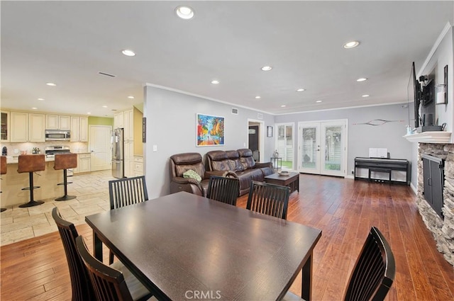 dining room featuring crown molding, a stone fireplace, light hardwood / wood-style floors, and french doors