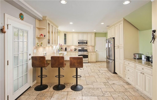 kitchen with a breakfast bar, appliances with stainless steel finishes, tasteful backsplash, light stone countertops, and cream cabinetry