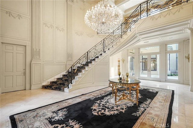 entryway featuring a towering ceiling, coffered ceiling, crown molding, an inviting chandelier, and french doors